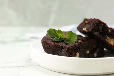 Photo of Delicious brownies with nuts and mint on white marble table, closeup. Space for text