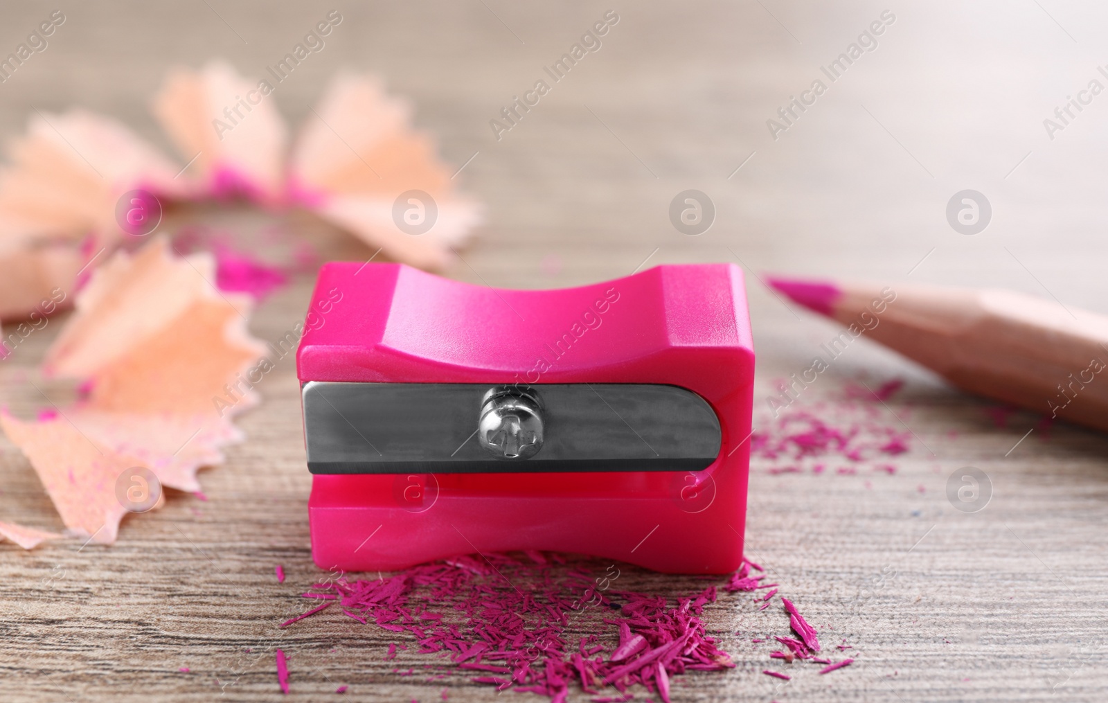 Photo of Pink sharpener, pencil and shavings on wooden table, closeup