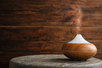 Photo of Modern essential oil diffuser on wooden table against brown background. Space for text