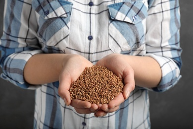 Woman holding raw buckwheat in hands on grey background, closeup