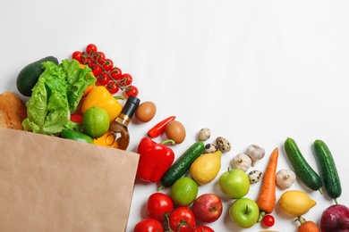 Paper bag with different groceries on white background, top view