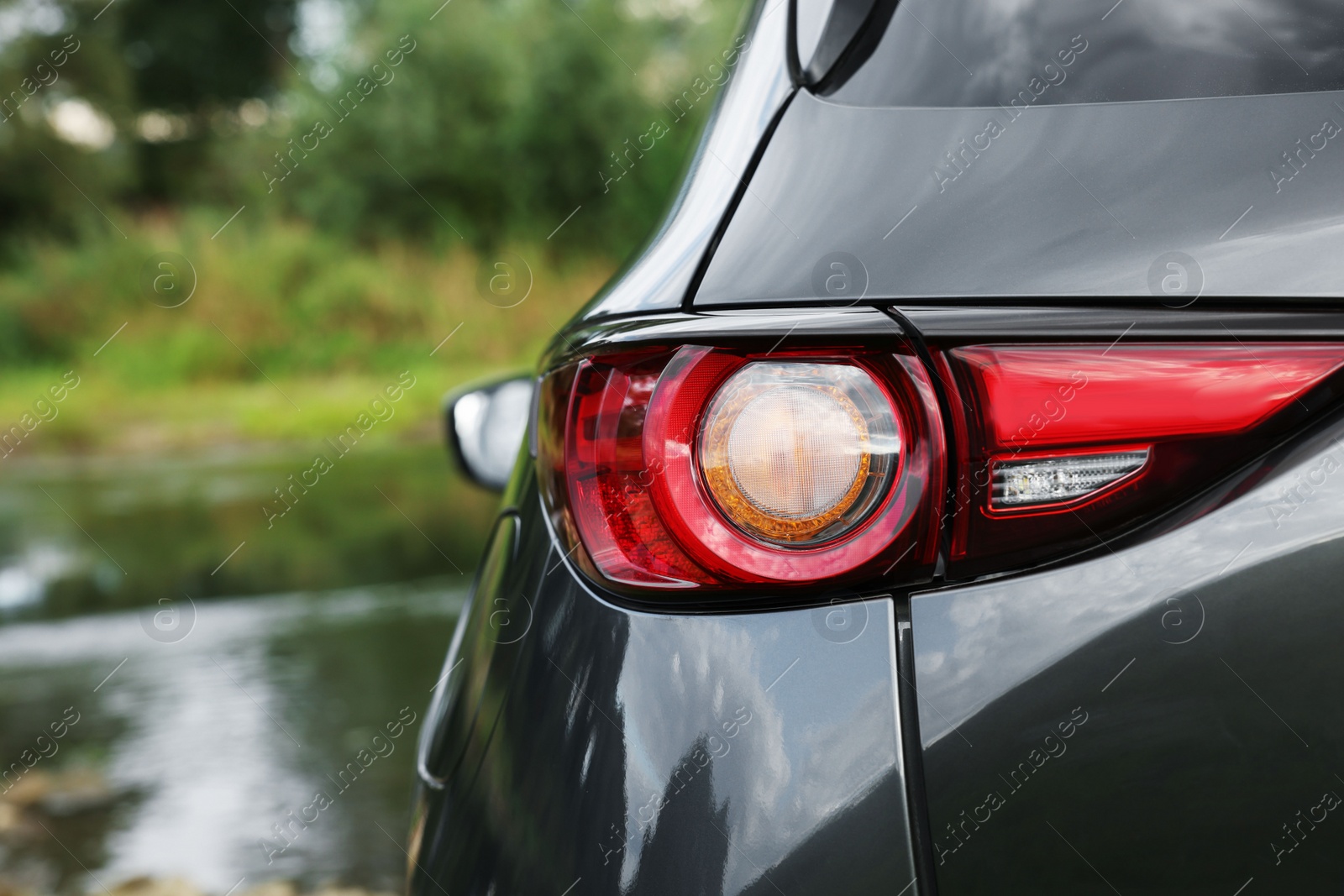 Photo of New black modern car near river, closeup of taillight. Space for text