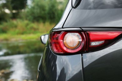 New black modern car near river, closeup of taillight. Space for text