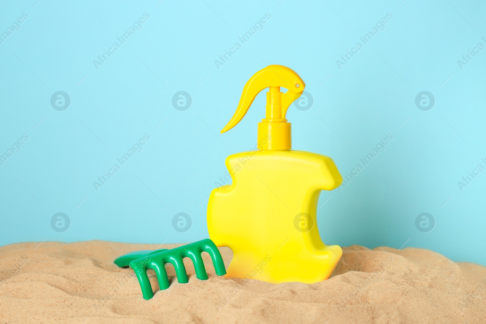 Photo of Suntan product and plastic beach toy on sand against light blue background