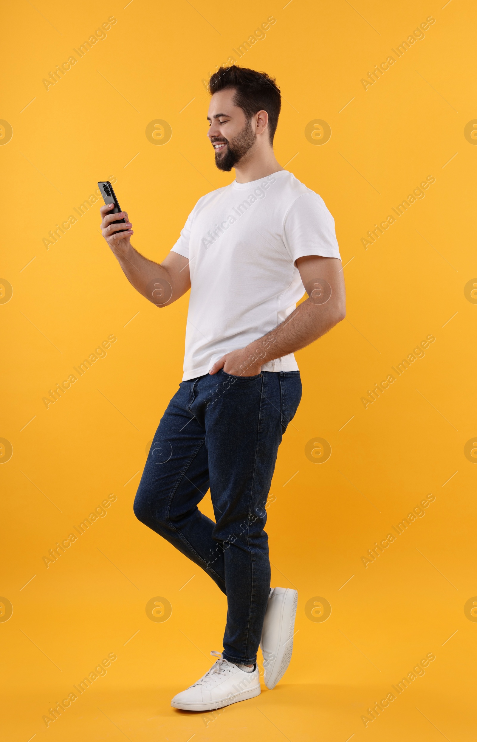 Photo of Happy young man using smartphone on yellow background