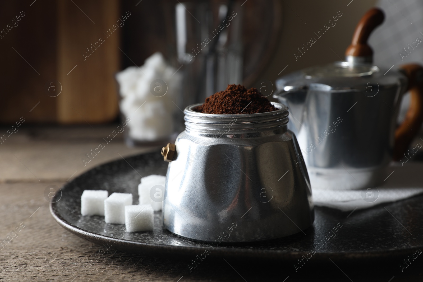 Photo of Ground coffee in moka pot and sugar cubes on wooden table, closeup