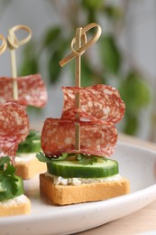 Photo of Tasty canapes with salami, cucumber and cream cheese on light table, closeup