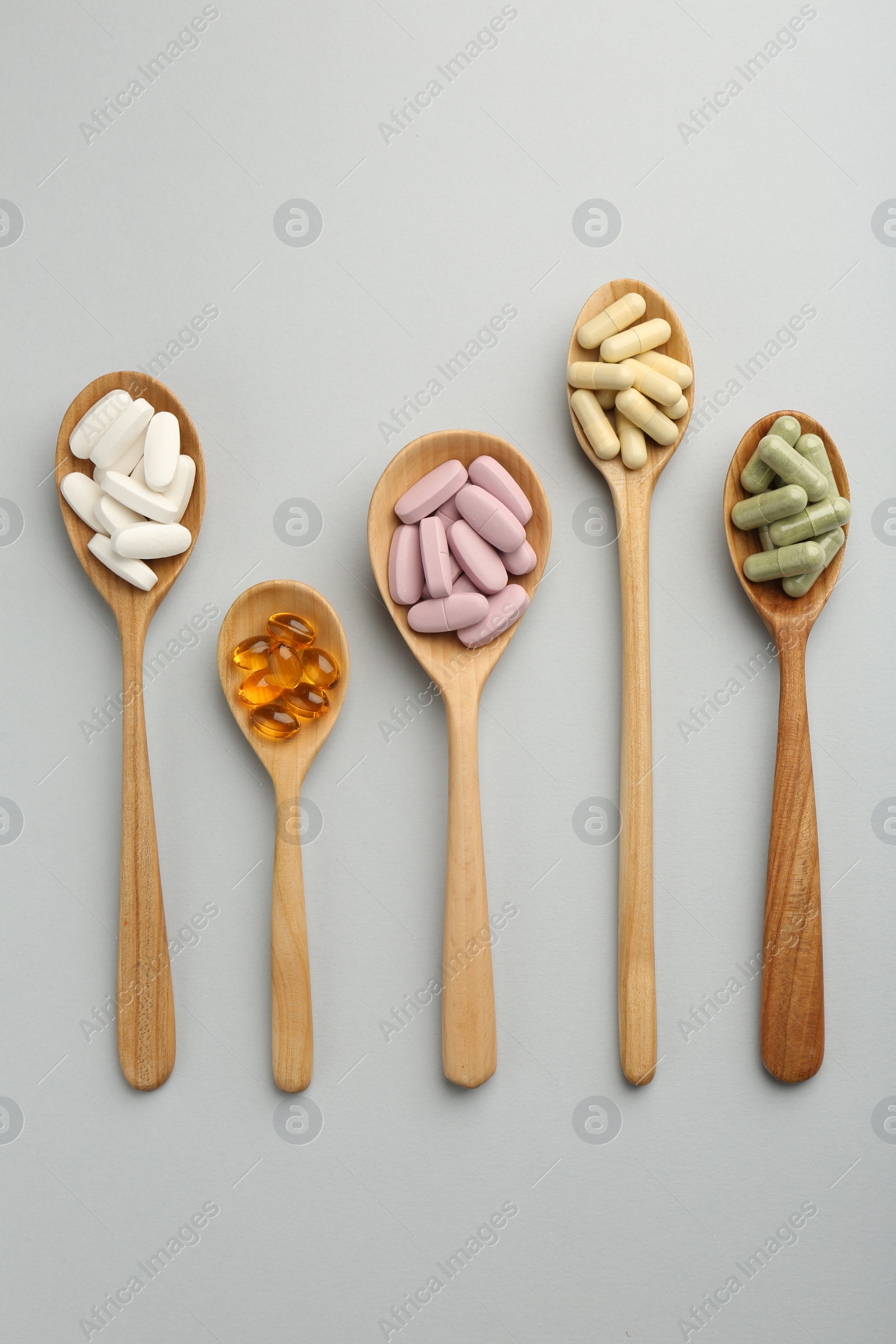 Photo of Different vitamin pills in spoons on light grey background, flat lay. Health supplement