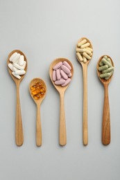 Photo of Different vitamin pills in spoons on light grey background, flat lay. Health supplement