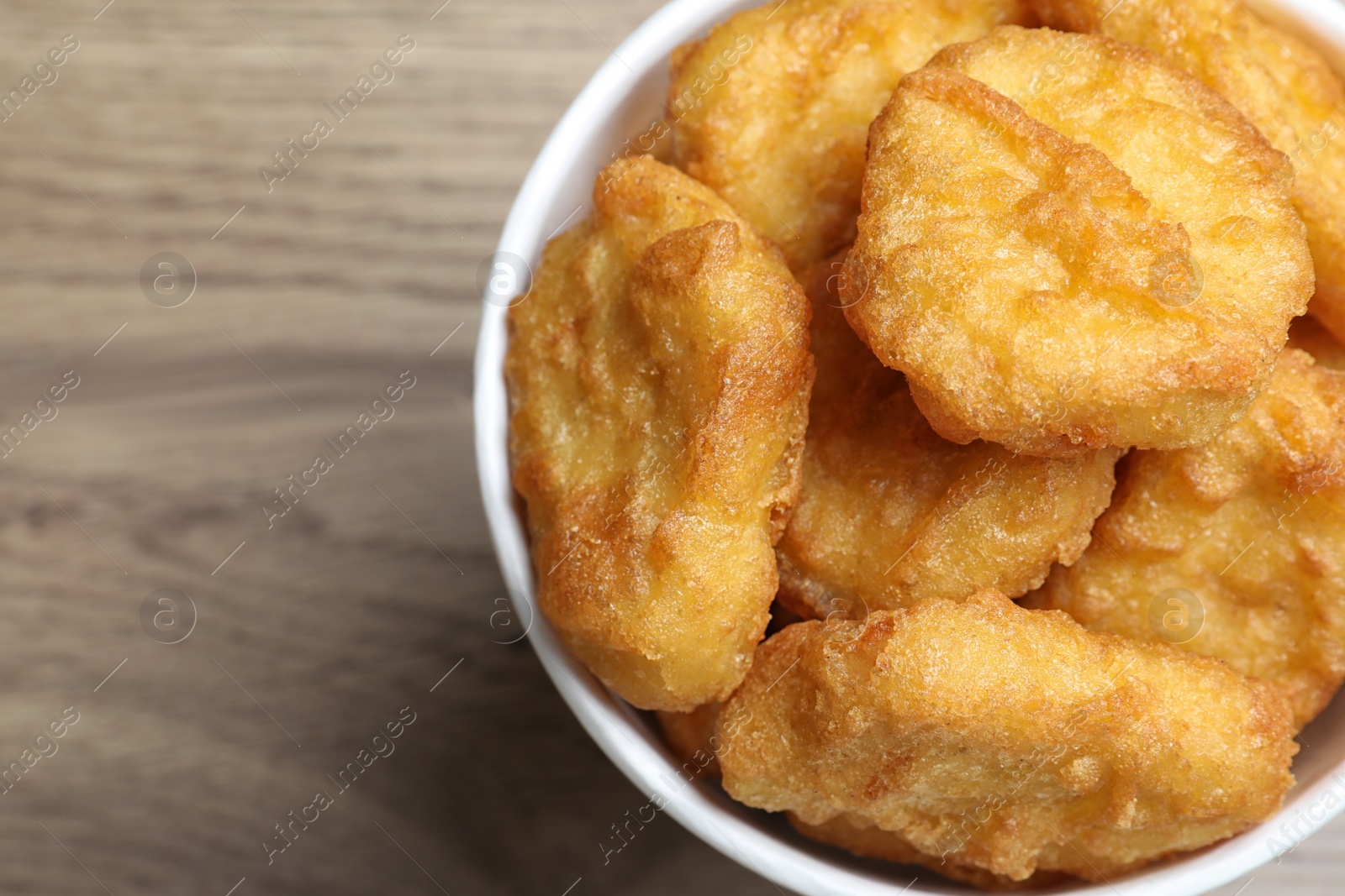 Photo of Bucket with tasty chicken nuggets on wooden table, top view