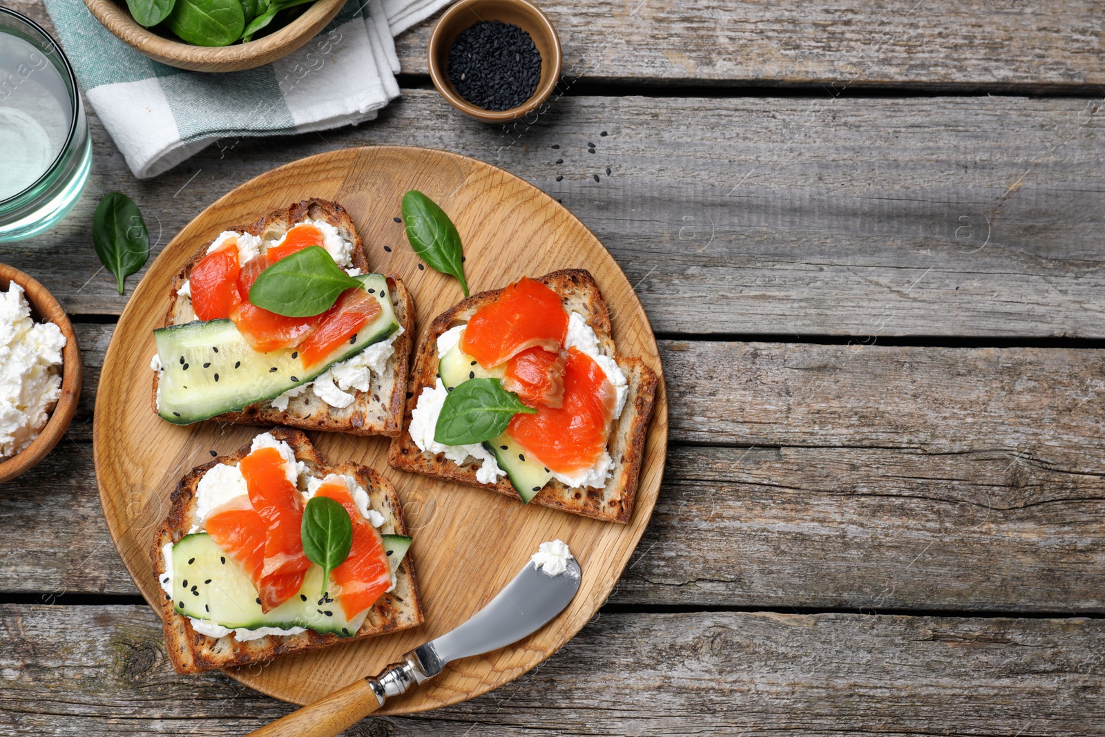 Photo of Delicious sandwiches with cream cheese, salmon, cucumber and spinach served on wooden table, flat lay. Space for text