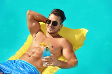 Young man with cocktail and inflatable mattress in pool on sunny day