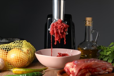 Photo of Electric meat grinder with minced beef and products on wooden table