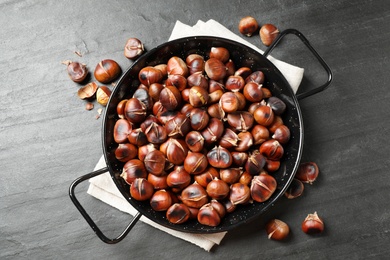 Photo of Delicious roasted edible chestnuts on black slate table, flat lay