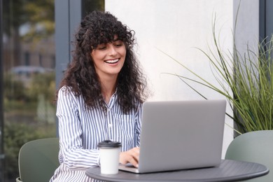 Photo of Happy young woman using modern laptop at table outdoors