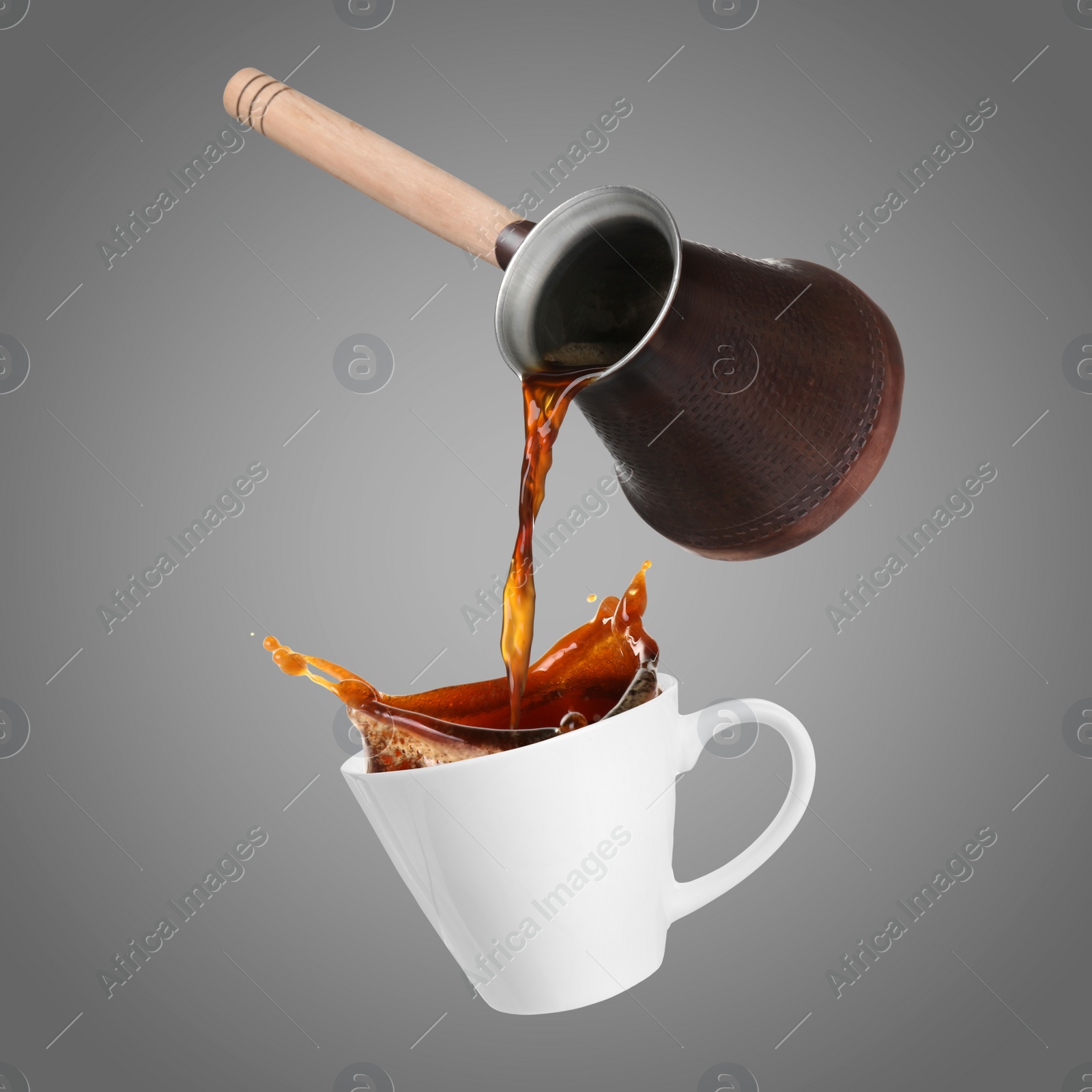 Image of Pouring freshly brewed aromatic coffee from turkish pot into cup. Objects in air on grey background