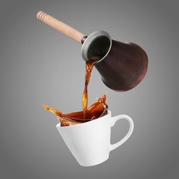 Pouring freshly brewed aromatic coffee from turkish pot into cup. Objects in air on grey background