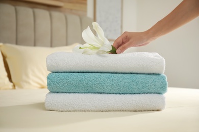 Photo of Woman putting flower on stack of clean towels in bedroom, closeup