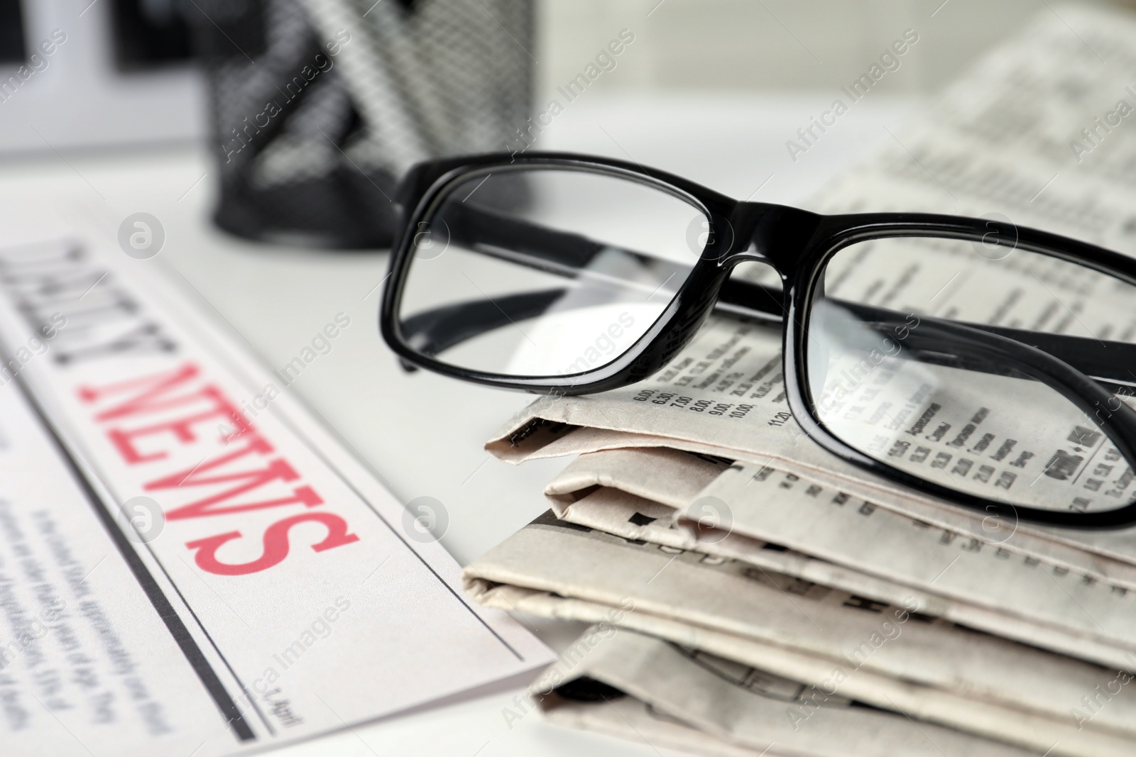 Photo of Stack of newspapers and glasses on white table, closeup