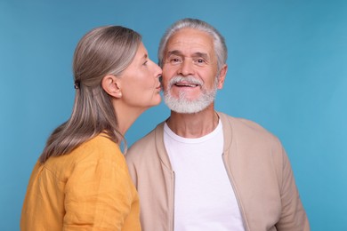 Senior woman kissing her beloved man on light blue background