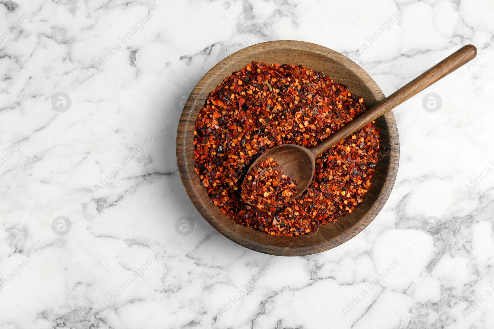 Photo of Plate with chili pepper flakes on marble background, top view