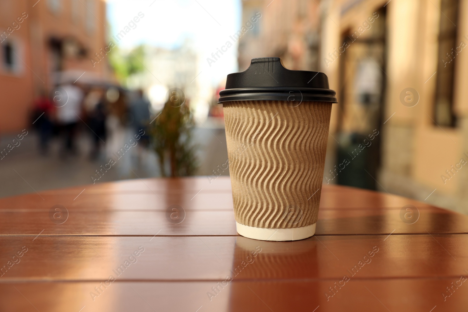 Photo of Cardboard takeaway coffee cup with plastic lid on wooden table in city, space for text