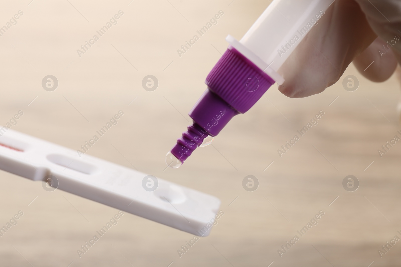 Photo of Doctor dropping buffer solution onto disposable express test cassette against blurred background, closeup