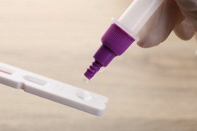 Doctor dropping buffer solution onto disposable express test cassette against blurred background, closeup