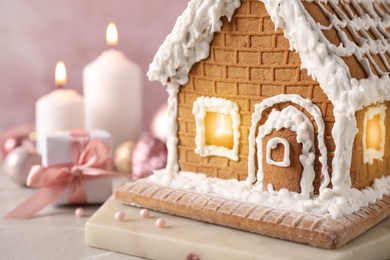 Photo of Beautiful gingerbread house decorated with icing on light table, closeup