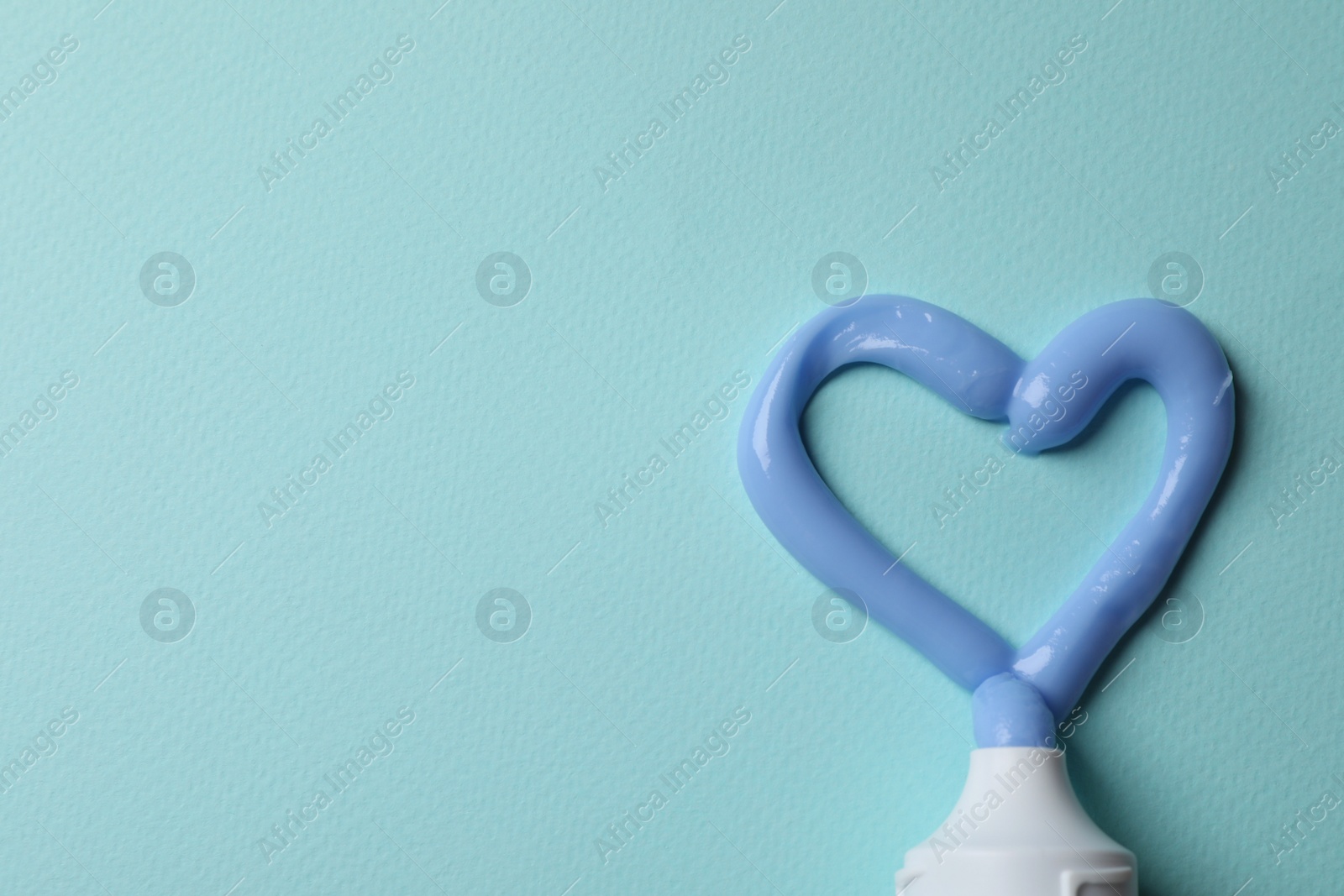 Photo of Heart made with toothpaste and tube on light blue background, flat lay. Space for text