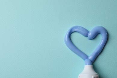 Photo of Heart made with toothpaste and tube on light blue background, flat lay. Space for text