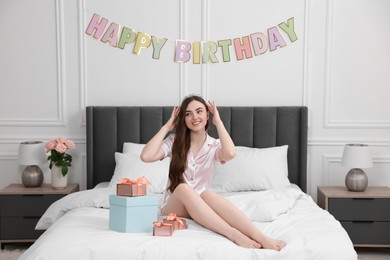 Photo of Beautiful young woman with headband and gift boxes on bed in room. Happy Birthday