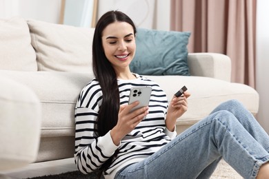 Photo of Happy young woman with credit card using smartphone for shopping online at home