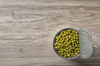 Photo of Open tin can of peas on wooden background, top view. Space for text