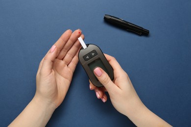 Photo of Diabetes. Woman checking blood sugar level with glucometer on blue background, top view