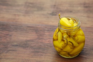 Photo of Glass jar of pickled yellow jalapeno peppers on wooden table. Space for text