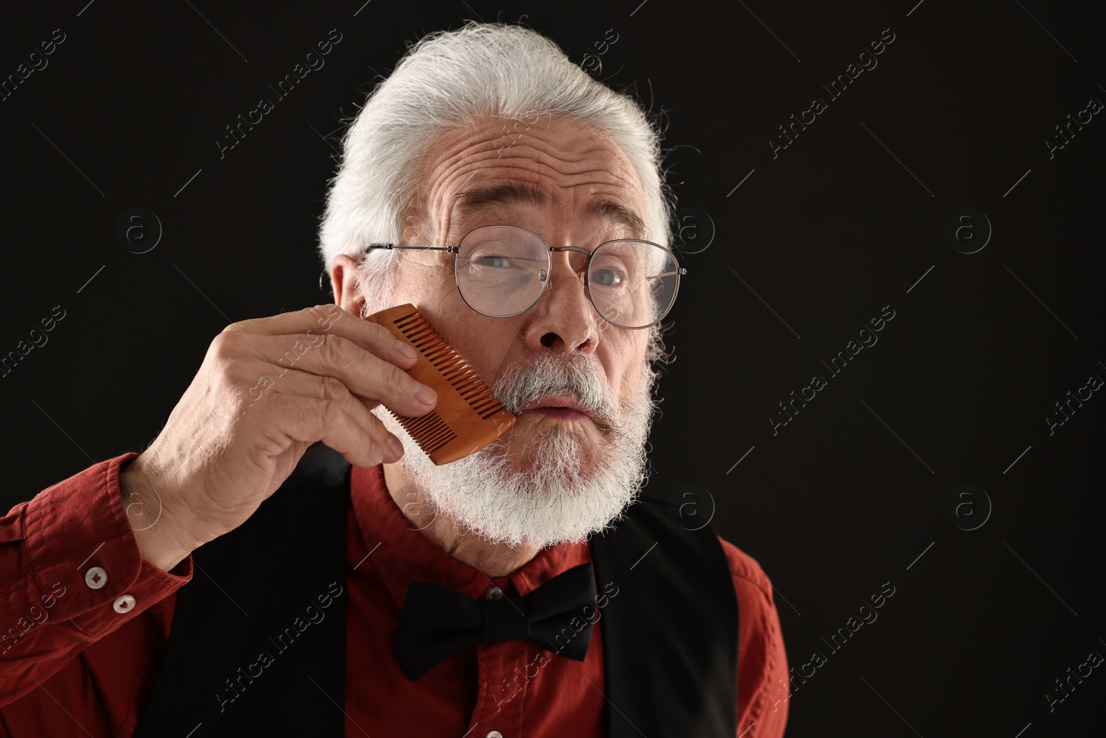 Photo of Senior man combing mustache on black background, space for text