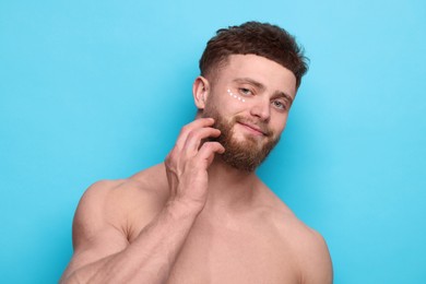 Photo of Handsome man with moisturizing cream on his face against light blue background