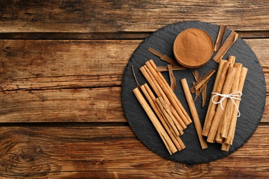 Photo of Aromatic cinnamon sticks and powder on wooden table, flat lay. Space for text