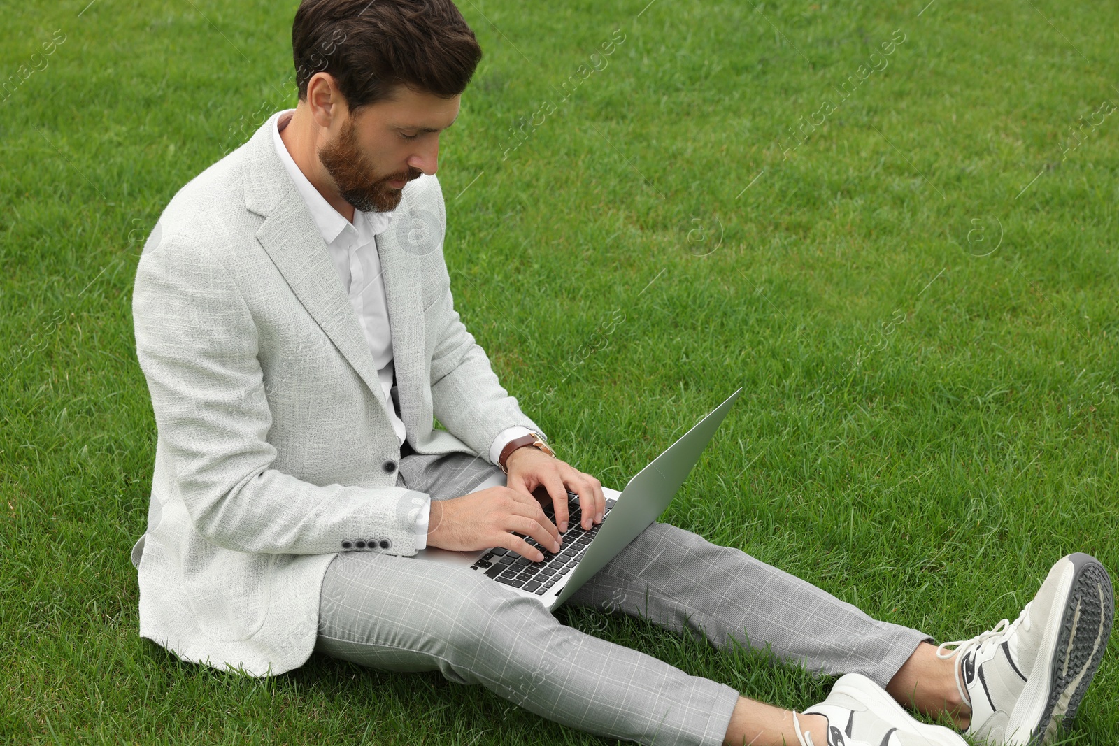 Photo of Handsome businessman with laptop on green grass outdoors