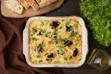 Photo of Tasty sausage casserole with green onions in baking dish on wooden table, flat lay