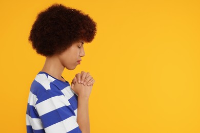 Woman with clasped hands praying to God on orange background. Space for text