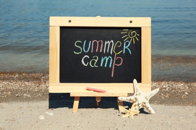 Photo of Small chalkboard with text SUMMER CAMP and starfish on beach near river