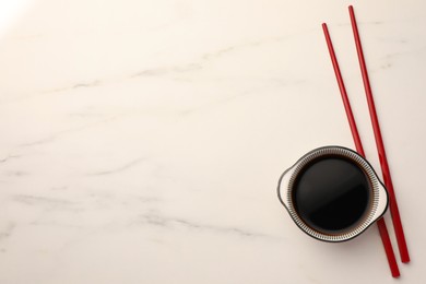 Photo of Bowl with soy sauce and chopsticks on white marble table, top view. Space for text