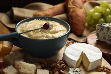 Photo of Fondue pot with tasty melted cheese, fork and different snacks on wooden table