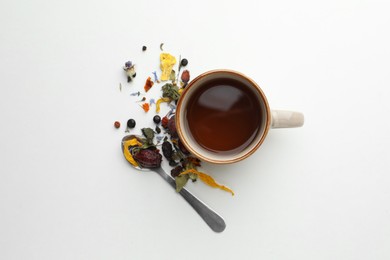 Cup of freshly brewed tea, dried herbs and spoon on white background, flat lay