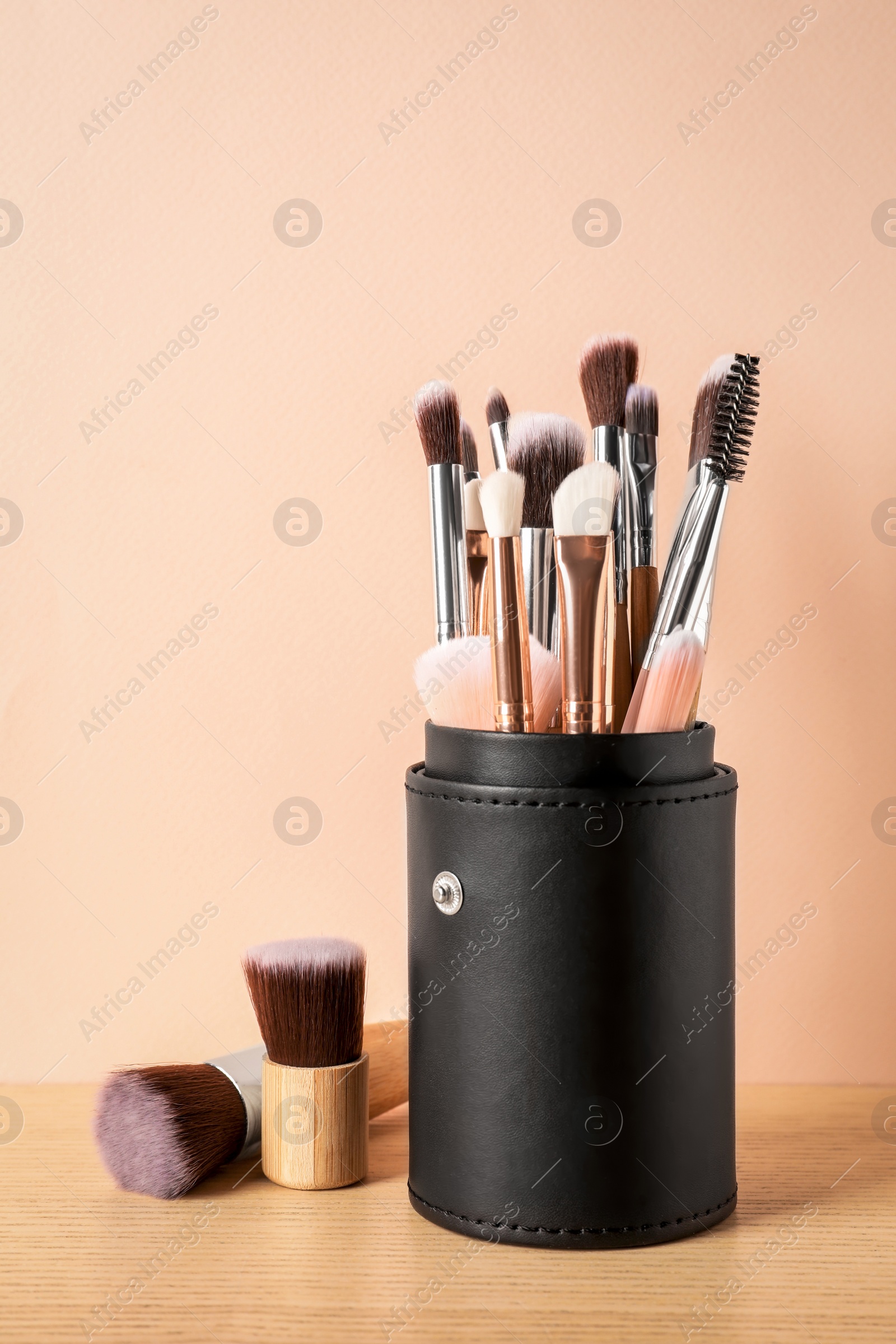 Photo of Set of professional makeup brushes on wooden table against beige background