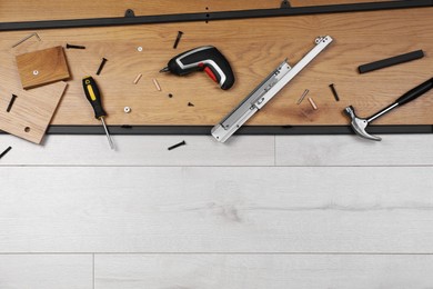 Flat lay composition with furniture assembly parts and tools on white wooden floor. Space for text