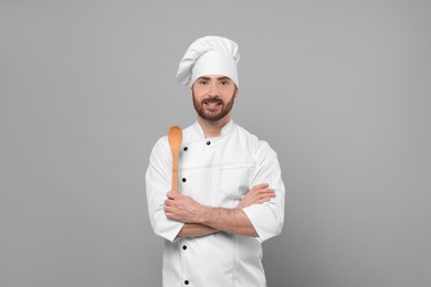 Photo of Smiling mature chef with spoon on grey background, space for text