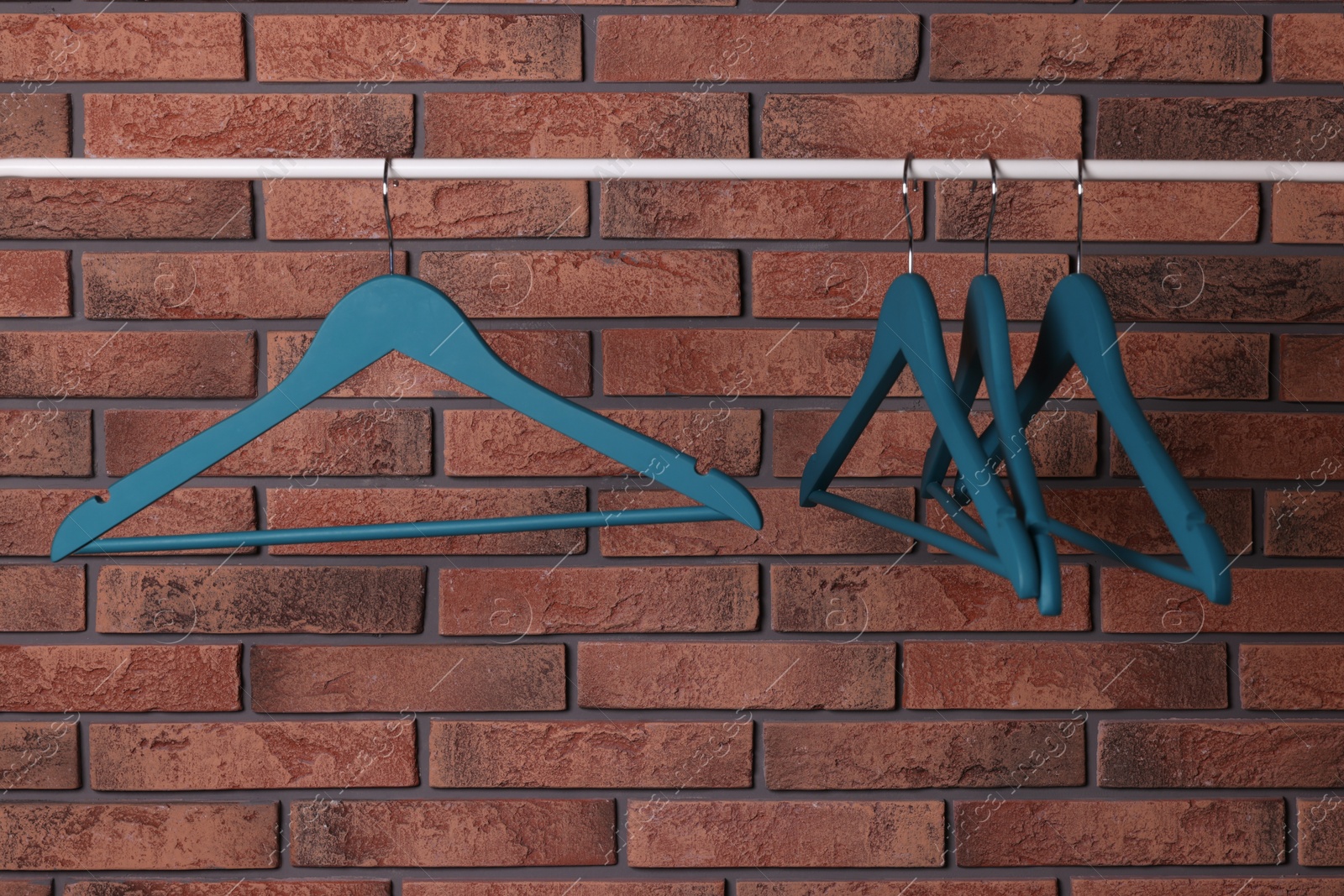 Photo of Blue clothes hangers on rail near red brick wall